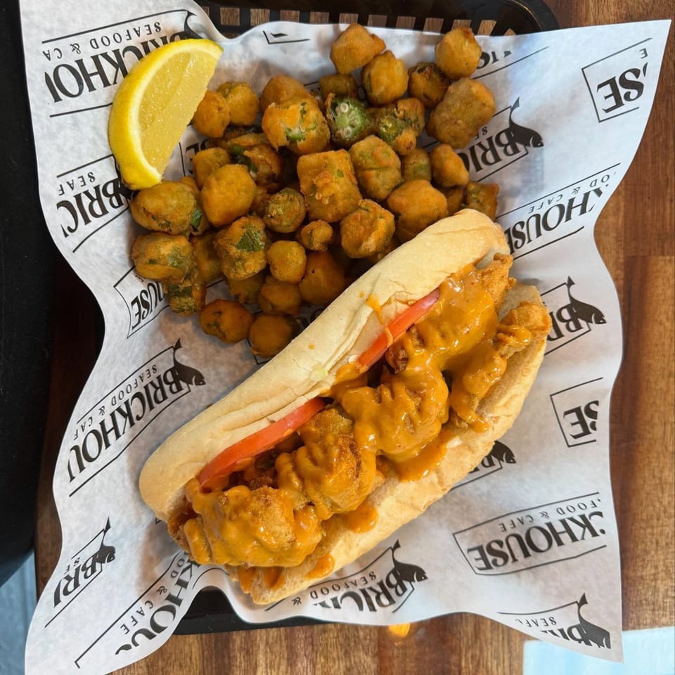 A Brickhouse Seafood Cafe shrimp po'boy with tomatoes and sauce, served with fried okra and a lemon wedge.