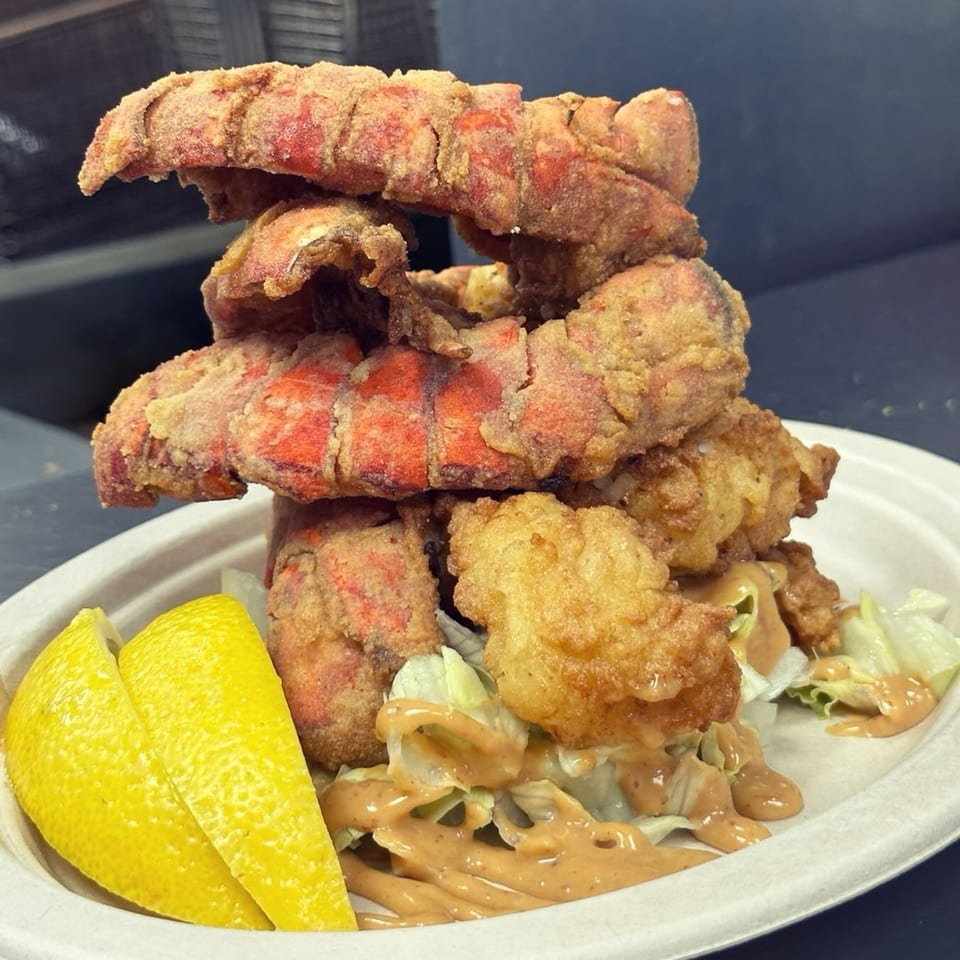 A towering stack of crispy fried lobster tails and shrimp, with lettuce, sauce, and lemon wedges.